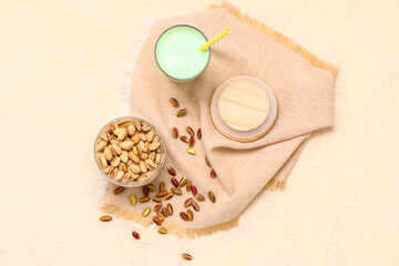 Fototapeta na wymiar Bowl with nuts, glass of pistachio milk and napkin on beige background