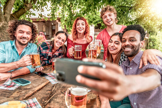 Happy friends drinking beer at outdoor brewery bar - Group of multiracial people taking selfie during ale toast - Friendship lifestyle concept young millennials having fun together at outdoor pub