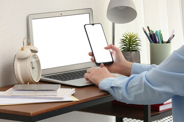Woman working with modern laptop and mobile phone at table in office