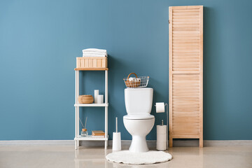 Interior of restroom with ceramic toilet bowl and shelving unit near blue wall