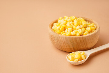 Bowl and spoon with canned corn kernels on beige background