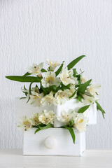 Drawers with beautiful alstroemeria flowers on table near light wall