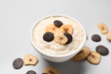 Bowl with delicious rice pudding, banana slices and chocolate chips on white background