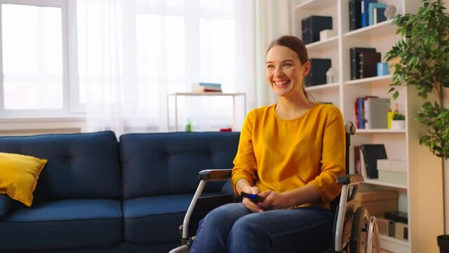 Cheerful young woman wheelchair user watching TV at home, entertainment time