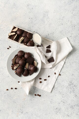 Plates with sweet chocolate bird's milk candies, coffee beans and jug of milk on light background