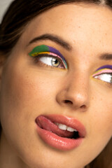 Naklejka premium Cropped view of teen model with multicolored makeup sticking out tongue.
