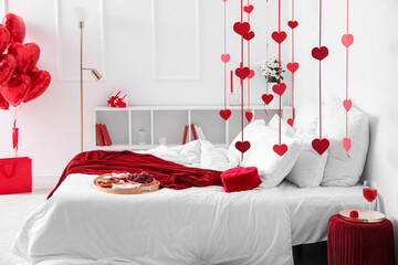 Interior of light bedroom decorated for Valentine's Day with breakfast, engagement ring and hearts