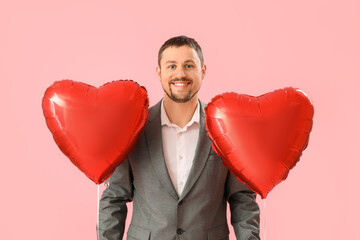 Handsome man with heart-shaped balloons on pink background. Valentine's Day celebration