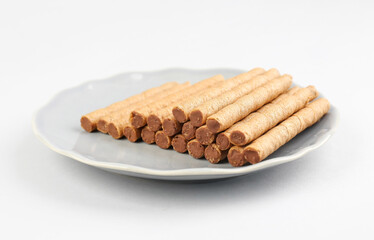Plate with heap of tasty wafer rolls on grey background