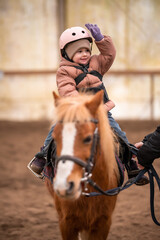 Fototapeta premium Little Child Riding Lesson. Three-year-old girl rides a pony and does exercises