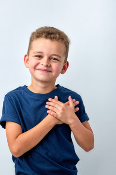 Close up of cute happy small boy isolated on white studio background hold hands at heart chest feel grateful, smiling little child pray thanking god high powers, faith concept