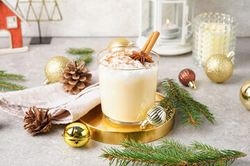 Glass of tasty eggnog cocktail, Christmas decorations and fir branches on table