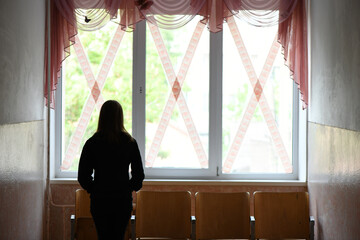 The girl stands at the school windows glued crosswise. War in Ukraine. High resolution photo.