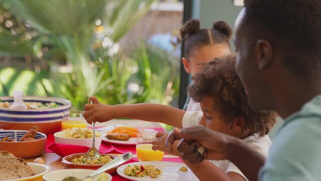 Multi-generation family sitting around table at home eating and enjoying meal together - shot in slow motion