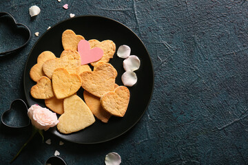 Plate with tasty heart shaped cookies and rose flower on dark color background. Valentines Day celebration