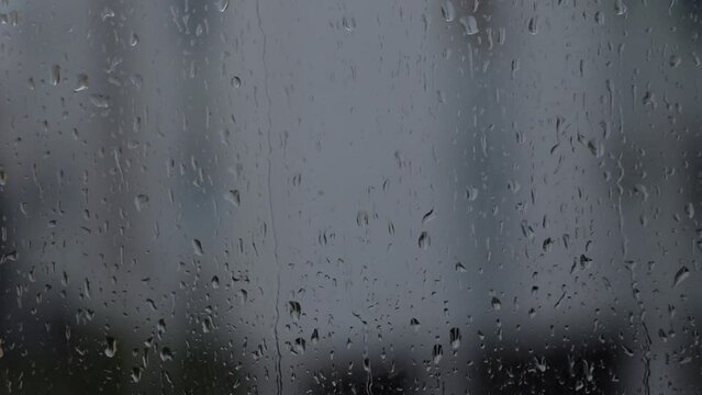 raindrops slowly running down the window glass, gray background