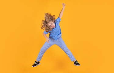 Funny boy jumping in air. Kid boy jump fly movement wear shirt and jeans isolated on yellow studio background.