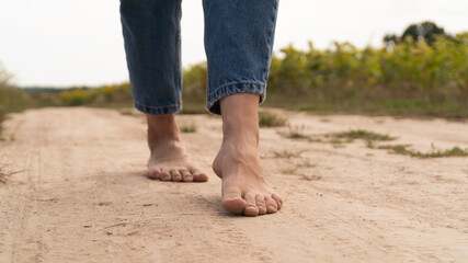 Woman walking in field meadow. Close-up of bare feet soiled with the ground.