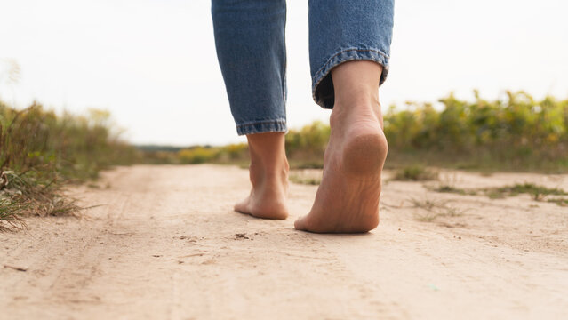 Woman walking in field meadow. Close-up of bare feet soiled with the ground.