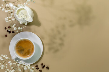 Cup of natural coffee, creamer with milk and coffee beans on beige background with white flowers...