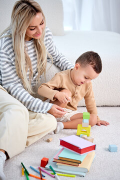 Happy Mother And Child Playing Game With Toys At Home Together, On Floor. Woman Looking After Little Kid. Cute Child Boy With Mom On Warm Floor In Modern Cozy Bright Room, Holidays And Weekends