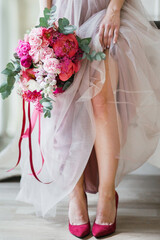 Bridesmaid dresses and pink shoes before the wedding ceremony. Wedding bouquet with pink peonies and roses. Closeup detail of bride putting on high heels sandals wedding shoes. 