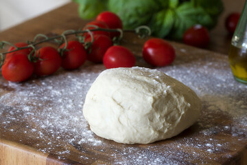 Fresh homemade pizza dough on a wooden cutting board with tomatoes and basil
