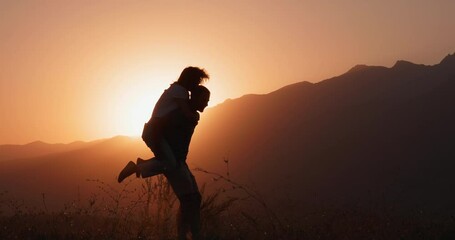 Silhouette view of a man spinning a woman on his back at sunset. A romantic date and love on nature of loving happy couple. 4k slowmotion - Powered by Adobe