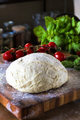 Fresh handmade pizza dough on a wood board with organic tomatoes and basil