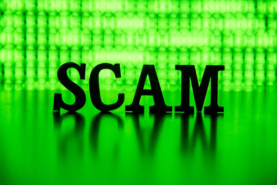 SCAM spelled out with letter tiles backlit by bright green binary code computer screen. - Powered by Adobe