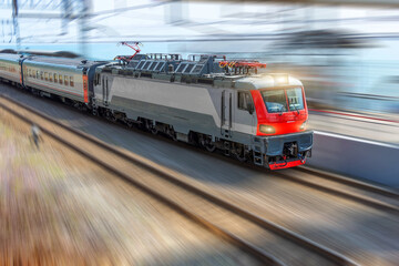 The electric locomotive head train rides with a train of passenger cars with a high speed along the rails.