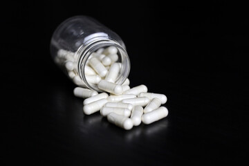 White pills on a black wooden table, medication in capsules scattered from the bottle. Background...