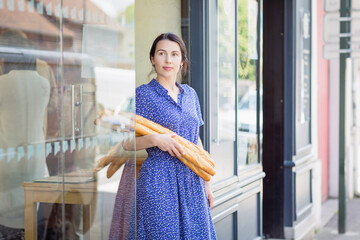 Young pretty woman buying a french baguette and standing on the street in city