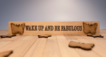 Wake up and be fabulous text. It is written on a wooden surface. The background is white.