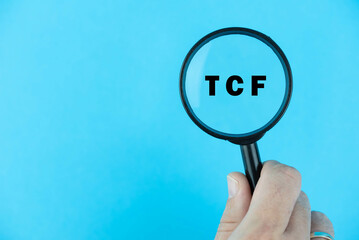 Focused on TCF exam. Word TCF (Test de connaissance du français) under magnifying glass. French Language Proficiency Test. Test Preparation. E-learning.