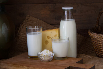 A bottle of milk, a glass of yogurt and kefir, cheese and some cottage cheese on a wooden background.