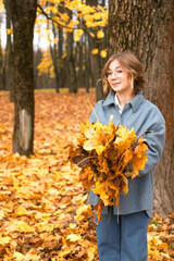 Vertical portrait of stylish, playful, smiling blond woman in eyeglasses holding bouquet of golden oak or maple leaves