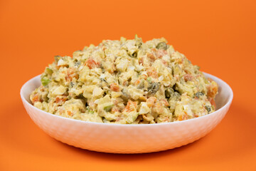 Olivier russian salad in a plate on an orange background close-up.