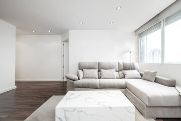 Living room of a short-term rental house with modern designer furniture in light wood and marble on a dark parquet floor and a gray fabric upholstered sofa with chaise longue