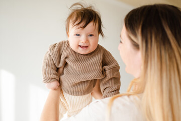 Happy laughing infant baby girl under 1 year old with young mother having fun in room closeup. Looking at camera. Motherhood.