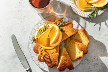 Sliced fluffy orange cake decorated with fresh orange slices on ceramic on light gray textured background, sunny morning breakfast in harsh light. Text space, flat lay, top view