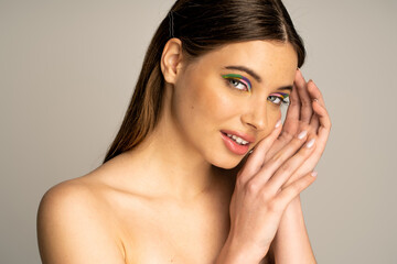 Smiling teen model with colorful makeup posing and looking at camera isolated on grey.