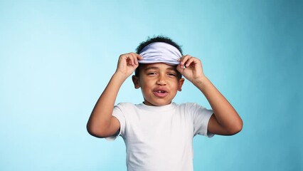 Cute sleepy little african american boy getting ready for bed with sleep mask or get up in the morning on isolated blue background Good night or morning  concept