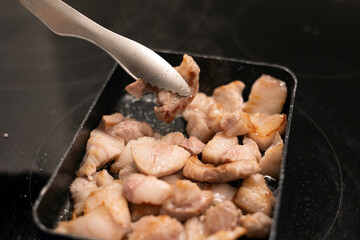 Cooking pork belly meat with frying pan and tongs