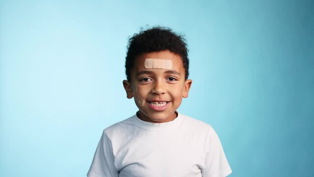 Portrait of clumsy smiling african american little boy with adhesive plaster looking at the camera on isolated blue background Happy childhood 