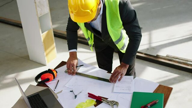 In front of the camera taking video of a man architect analysing and make some measurements of the plan of construction he using a pencil to make the notes