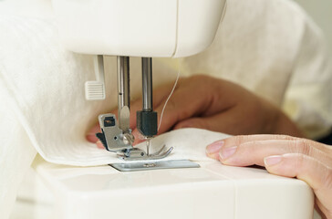 A female seamstress sews white fabric items on a sewing machine.