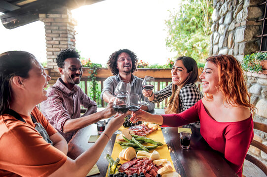 Millenial friends having fun drinking and toasting red wine at lunch party on sunny day - Young people eating local food at restaurant winery together - Dining lifestyle concept