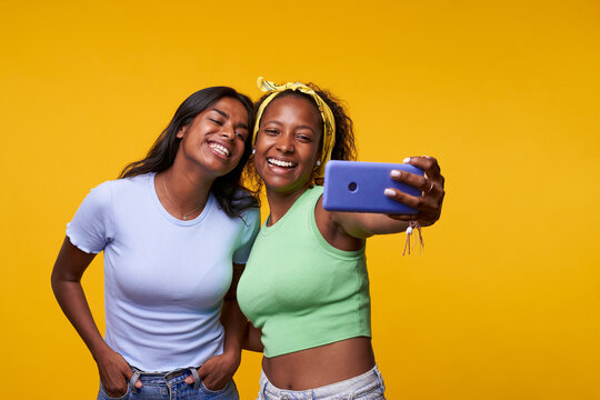 Portrait of cool cheerful girl having video call with lover holding smart phone in hand shooting selfie on front camera isolated on yellow background enjoying happy moment. 