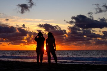 Fototapeta premium Two female friends taking photos at sunset on the beach
